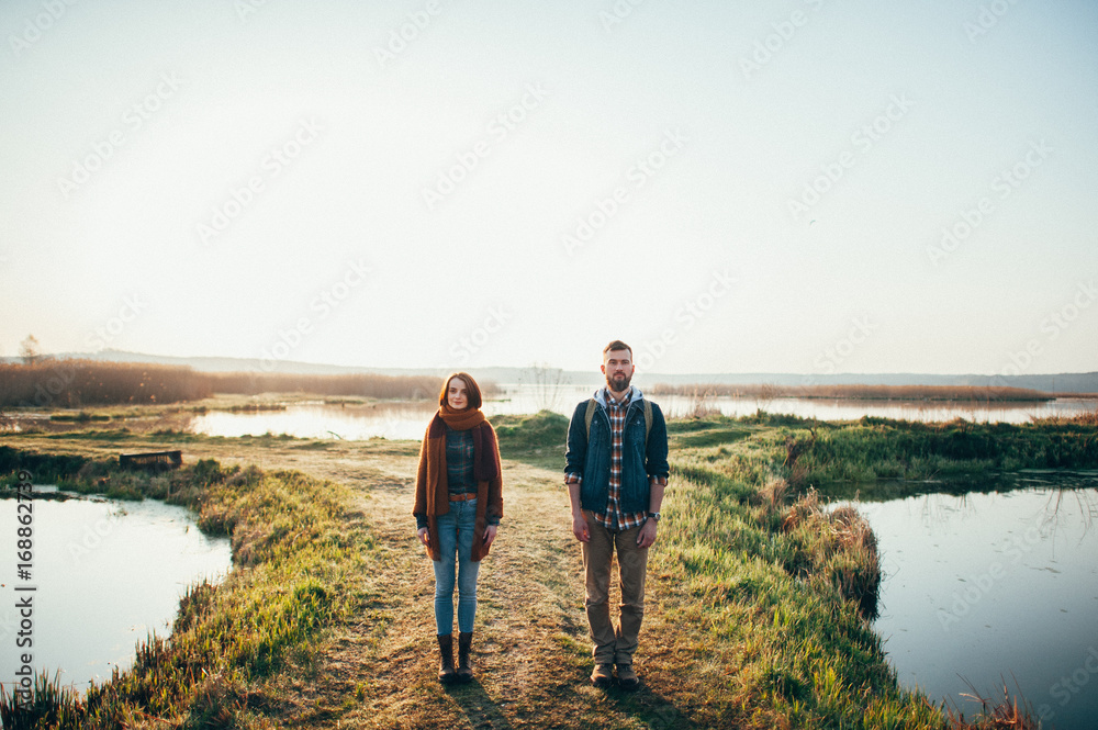 man and woman standing with canoe and paddle on coast of lake in sunny morning