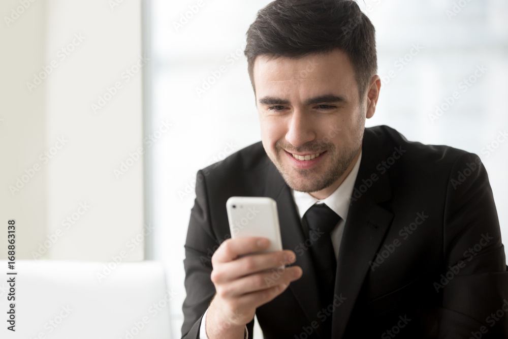 Attractive smiling businessman looking at smartphone in his hand, texting, sending messages on cellphone, using easy banking app, checking daily calendar or personal organizer, mobile office. Portrait Attractive smiling businessman looking at smartphone in his hand, texting, sending messages on cellphone, using easy banking app, checking daily calendar or personal organizer, mobile office. Portrait
