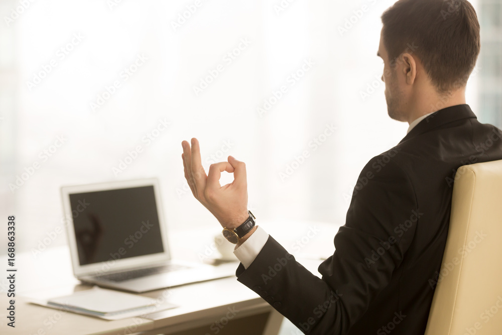 Close up of hand in chin mudra yogic gesture, mindful calm yogi businessman meditating at workplace near laptop, doing yoga exercise, practicing breathing, meditation at work, no stress, back view
