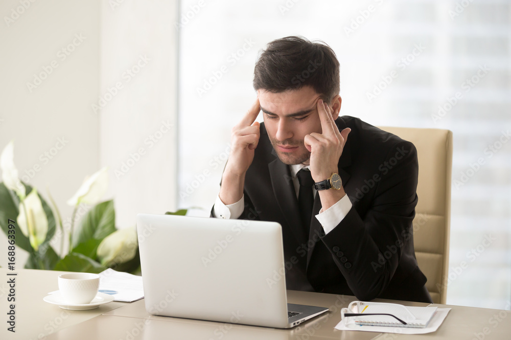 Serious frustrated businessman with closed eyes suffering from headache migraine at workplace, massaging temples, feeling tired exhausted, chronic work stress, tries to remember important information Serious frustrated businessman with closed eyes suffering from headache migraine at workplace, massaging temples, feeling tired exhausted, chronic work stress, tries to remember important information