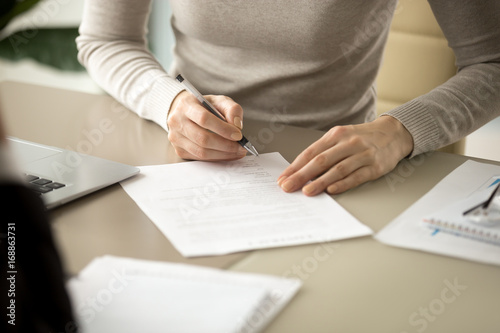 Woman signing document, focus on female hand holding pen, putting signature at official paper, subscribing name in statement with legal value, contract management, good business deal, close up view photo