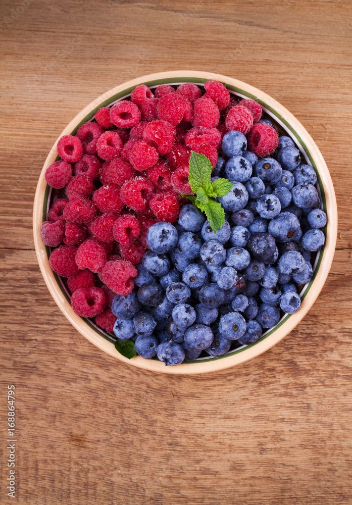Blueberries and raspberries in clay bowl. Freshly picked berries on rustic background. Berry antioxidant superfood, concept for healthy eating. View from above, top studio shot Blueberries and raspberries in clay bowl. Freshly picked berries on rustic background. Berry antioxidant superfood, concept for healthy eating. View from above, top studio shot