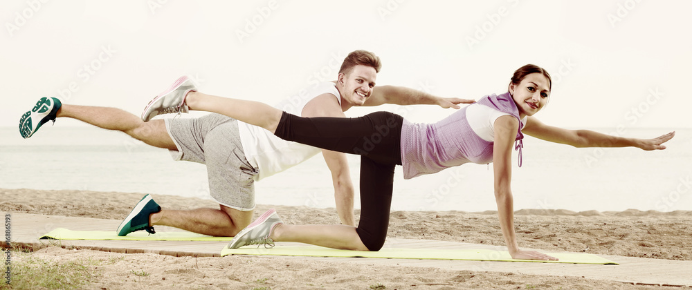 guy and girl practising yoga poses sitting on beach by sea at daytime