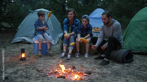 travel in camp, Mom, children and dad around fire roasting corn, family evening picnic outdoors, American family during summer holidays, mother, father and sons on rest in forest photo