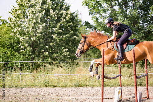 Young female jockey on horse leaping over hurdle