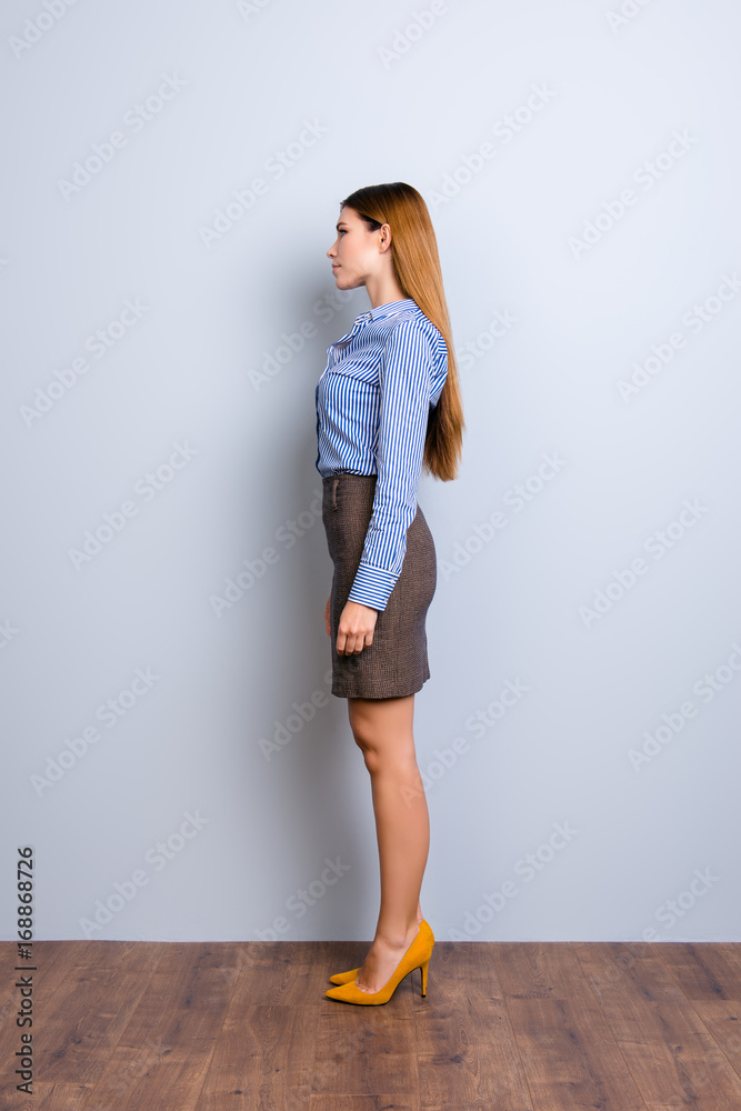 Full length profile portrait of serious young business lady in strict formal wear, standing still on light background in pump shoes Full length profile portrait of serious young business lady in strict formal wear, standing still on light background in pump shoes
