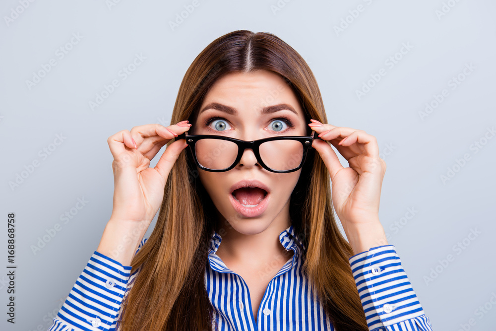 No way! Really?! Shocked blond attractive girl in glasses is holding them with her fingers. She is amazed and with open mouth on pure light grey background No way! Really?! Shocked blond attractive girl in glasses is holding them with her fingers. She is amazed and with open mouth on pure light grey background