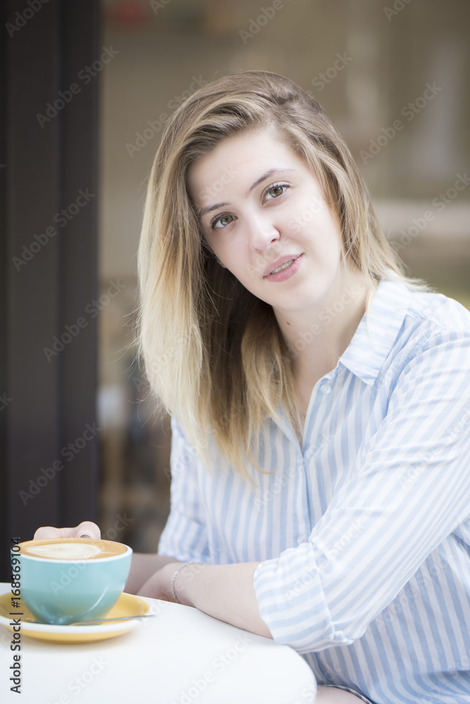 Beautiful blonde girl at a table in a cafe with a cup of coffee