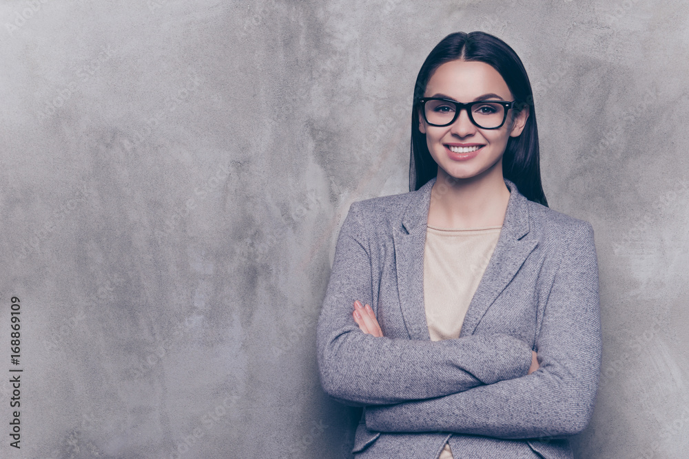 Beautiful woman in spectacles with beaming smile standing with crossed hands against gray background Beautiful woman in spectacles with beaming smile standing with crossed hands against gray background