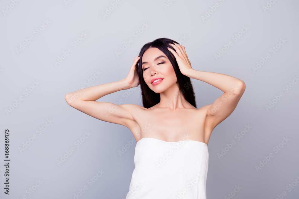 Beautiful young asian girl, wrapped in a white towel is touching her hair on light grey background, so charming and happy Beautiful young asian girl, wrapped in a white towel is touching her hair on light grey background, so charming and happy