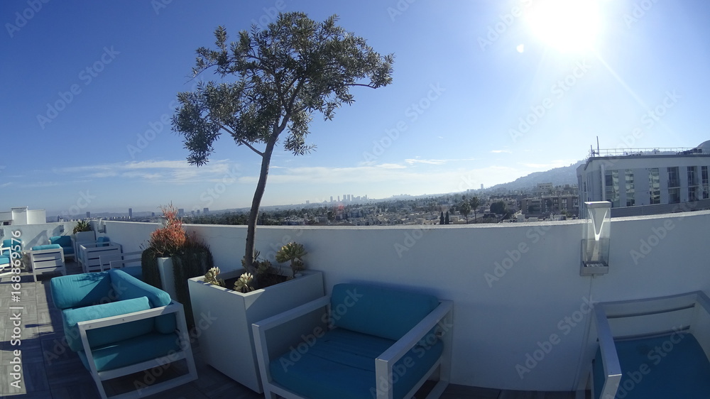A rooftop lounge with blue sitting chairs, on the roof of a residential building, with a panoramic view of Los Angeles in the background.