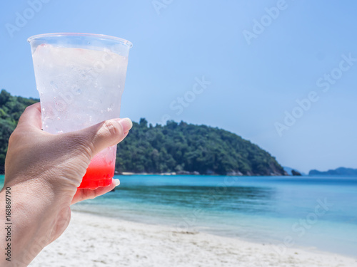 Tropical cocktail in woman  s hand with seascape background.