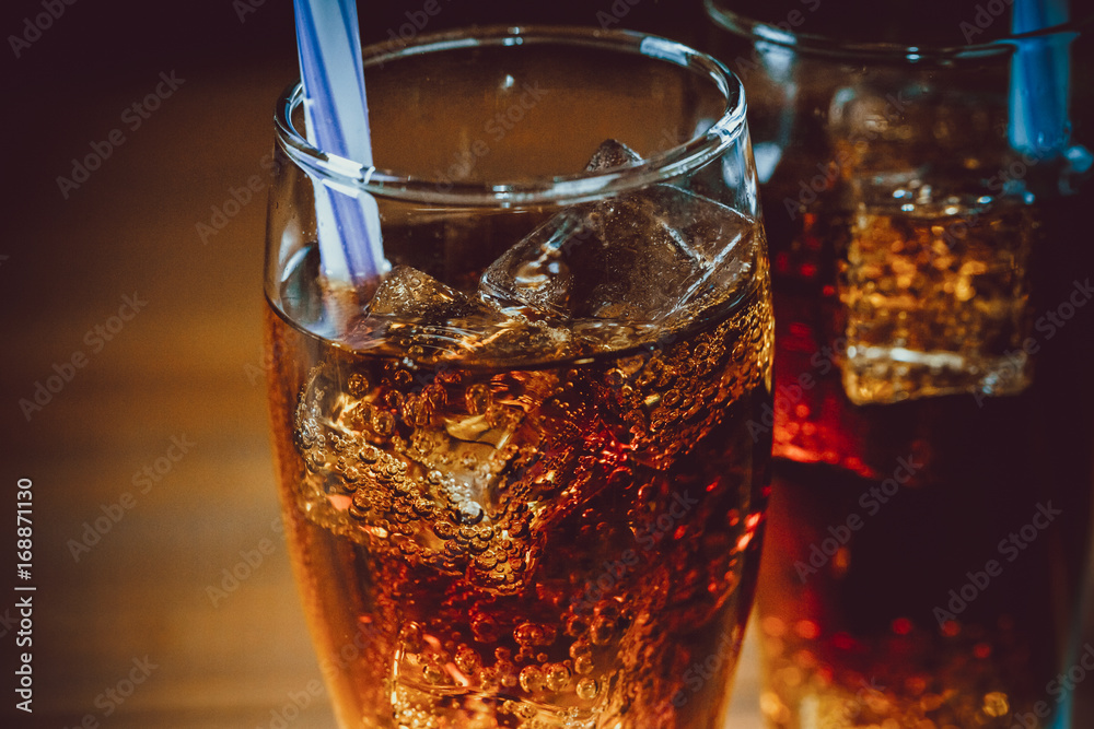 Beautiful cold drink of Cola with ice cubes with a boiler straws in glasses on wooden background with free space. Shallow DOF. Beautiful cold drink of Cola with ice cubes with a boiler straws in glasses on wooden background with free space. Shallow DOF.