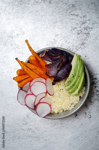 Fresh healthy vegetarian bowl for lunch with baked carrots and red onion, coucous and sliced avocado. Simple and colourful organic food concept. Minimalistic flat lay with copy space. photo