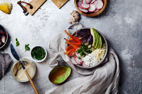 Fresh healthy vegetarian bowl for lunch with baked carrots and red onion, coucous and sliced avocado. Simple and colourful organic food concept. Flat lay with copy space.