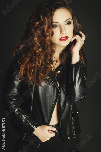 Beautiful young woman posing in black leather jacket over grey background. Fashion concept.