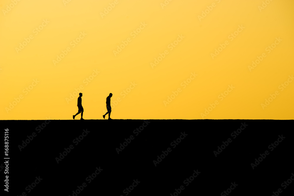 Picture of two men silhouettes walking in the sunset Picture of two men silhouettes walking in the sunset