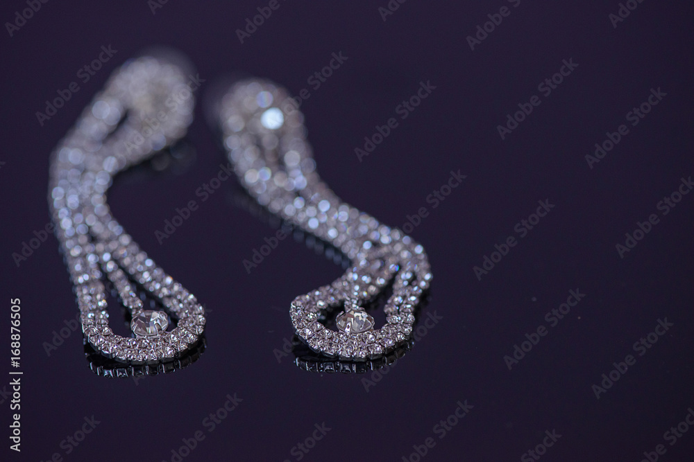 Fake diamonds double row prong setting mount hanging earrings with selective focus, positioned on a dark blue glossy surface