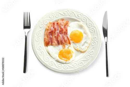 Plate with fried eggs  bacon and cutlery on white background
