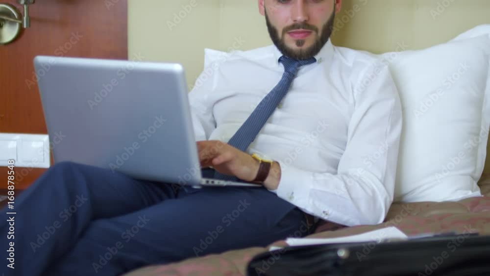 Tilt up of young businessman in formal shirt and tie lying on bed in ...