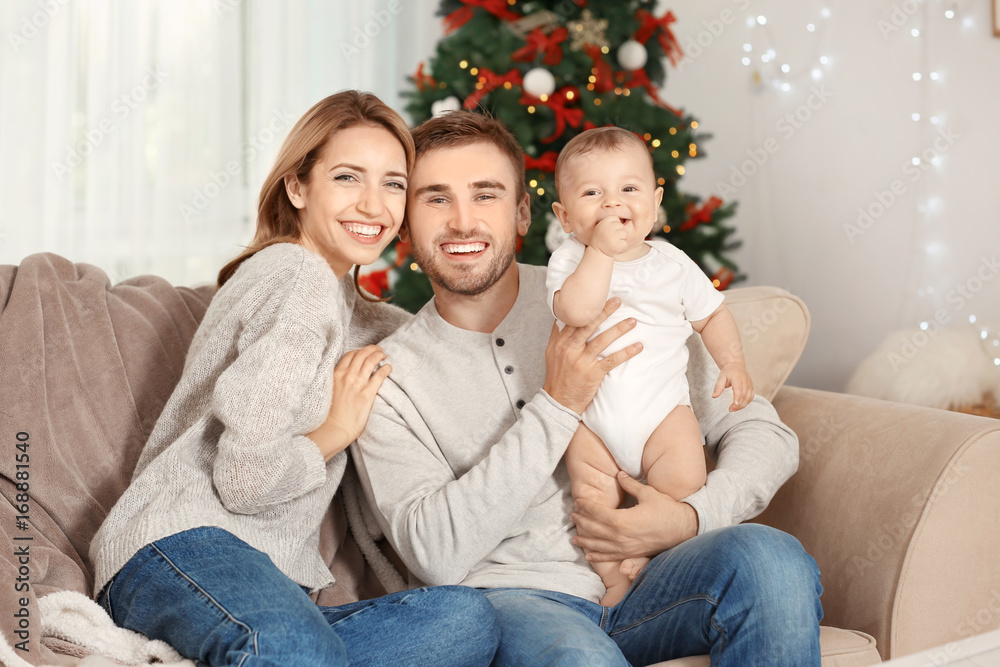 Happy parents with baby in decorated room for Christmas