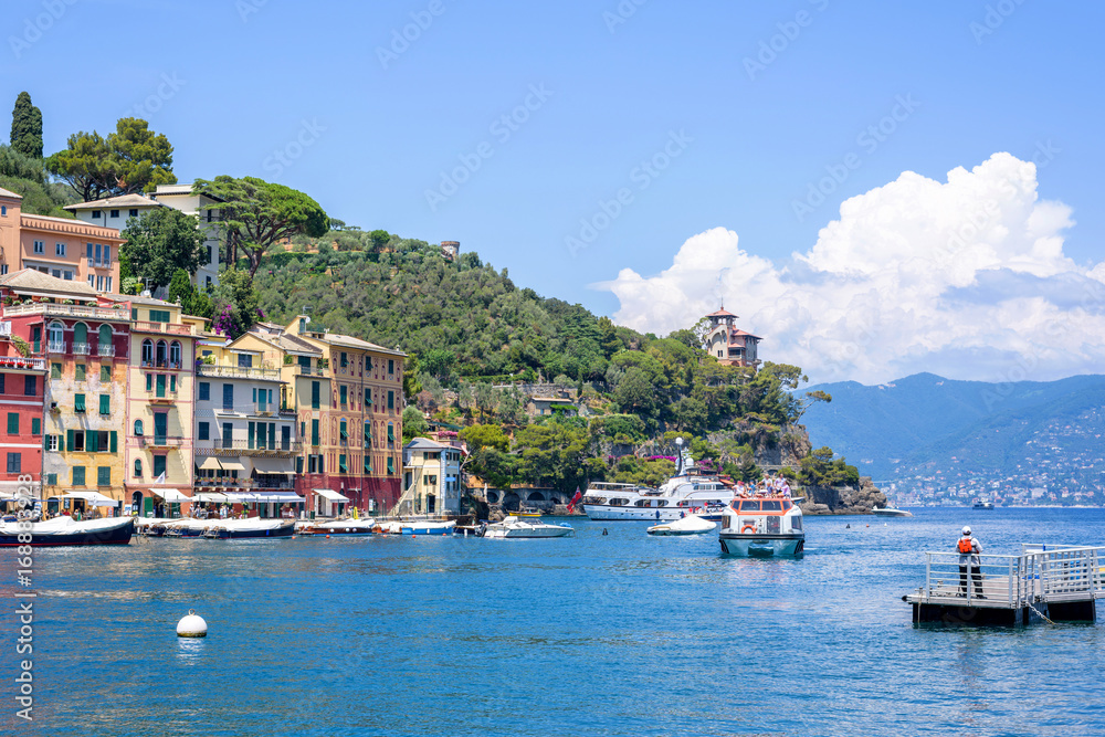 Beautiful daylight view to ships on water and buildings in Portofino city of Italy. Tourists walking on sidewalk.