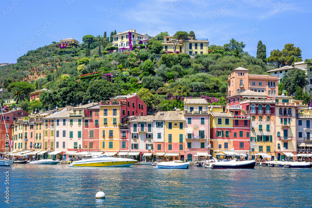 Beautiful daylight view to ships on water and buildings in Portofino city of Italy. Tourists walking on sidewalk.