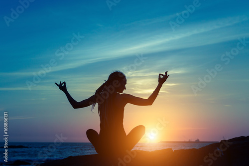 Yoga and healthy lifestyle background, silhouette of woman meditating on the sea beach.