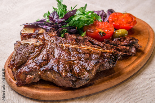 Appetizing steak on the bone, with tomatoes and herbs, on a wooden board. Horizontal frame