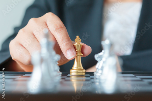 Close up shot hand of business woman holding golden chess between row of silver chess on white and black chess board for business challenge competition winner and loser concept