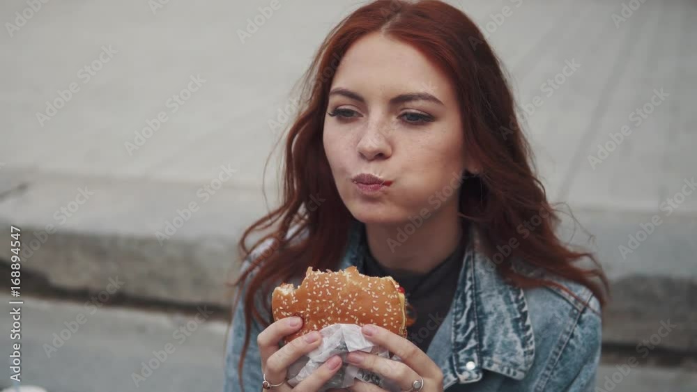 redhead girl enjoy tasty bites delicious sandwich and smiles slyly. 20s redhead girl enjoy tasty bites delicious sandwich and smiles slyly. 20s