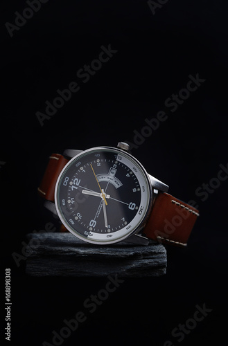 Wrist watch with a black dial on a gray stone with a dark background.