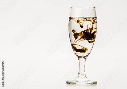 Dark brown food coloring diffuse in water inside wine glass with empty copyspace area for slogan or advertising text message, over isolated grey background. 