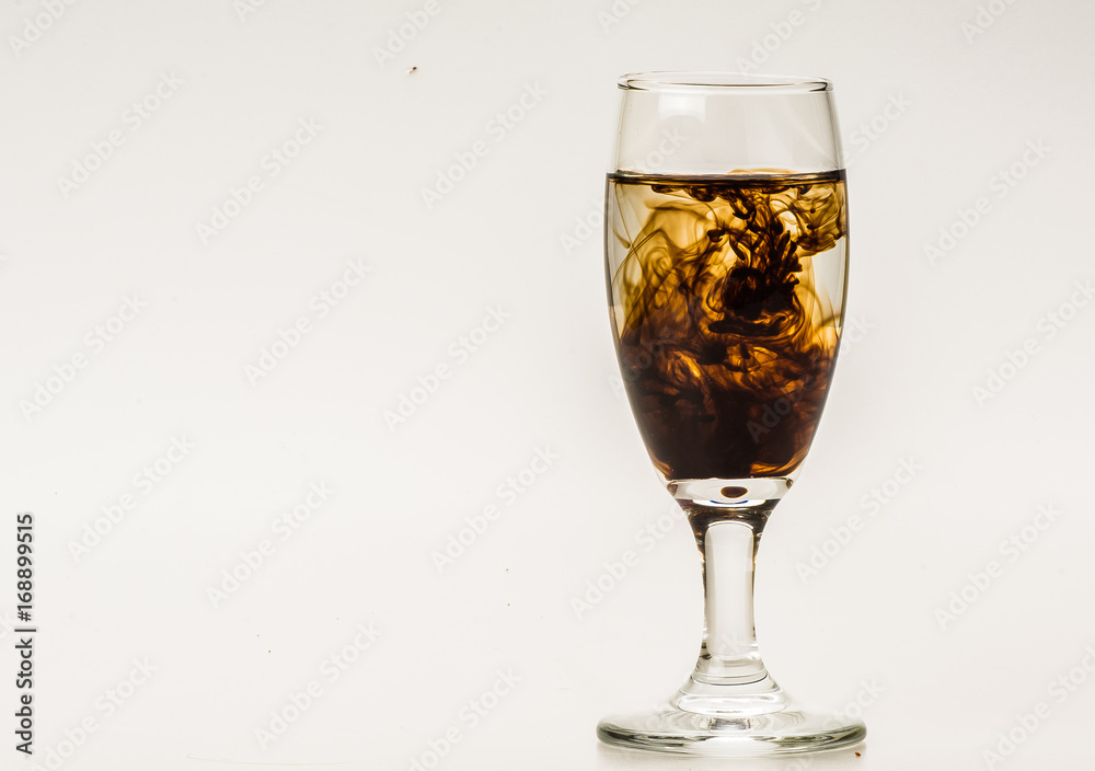Dark brown food coloring diffuse in water inside wine glass with empty copyspace area for slogan or advertising text message, over isolated grey background. Dark brown food coloring diffuse in water inside wine glass with empty copyspace area for slogan or advertising text message, over isolated grey background.