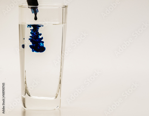 Blue food coloring diffuse in water inside glass with empty copyspace area for slogan or advertising text message, over isolated grey background. 