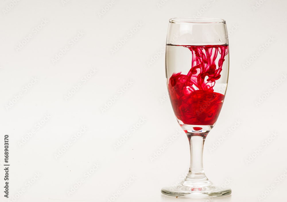 Red food coloring diffuse in water inside wine glass with empty copyspace area for slogan or advertising text message, over isolated grey background. Red food coloring diffuse in water inside wine glass with empty copyspace area for slogan or advertising text message, over isolated grey background.