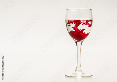 Red food coloring diffuse in water inside wine glass with empty copyspace area for slogan or advertising text message, over isolated grey background. 