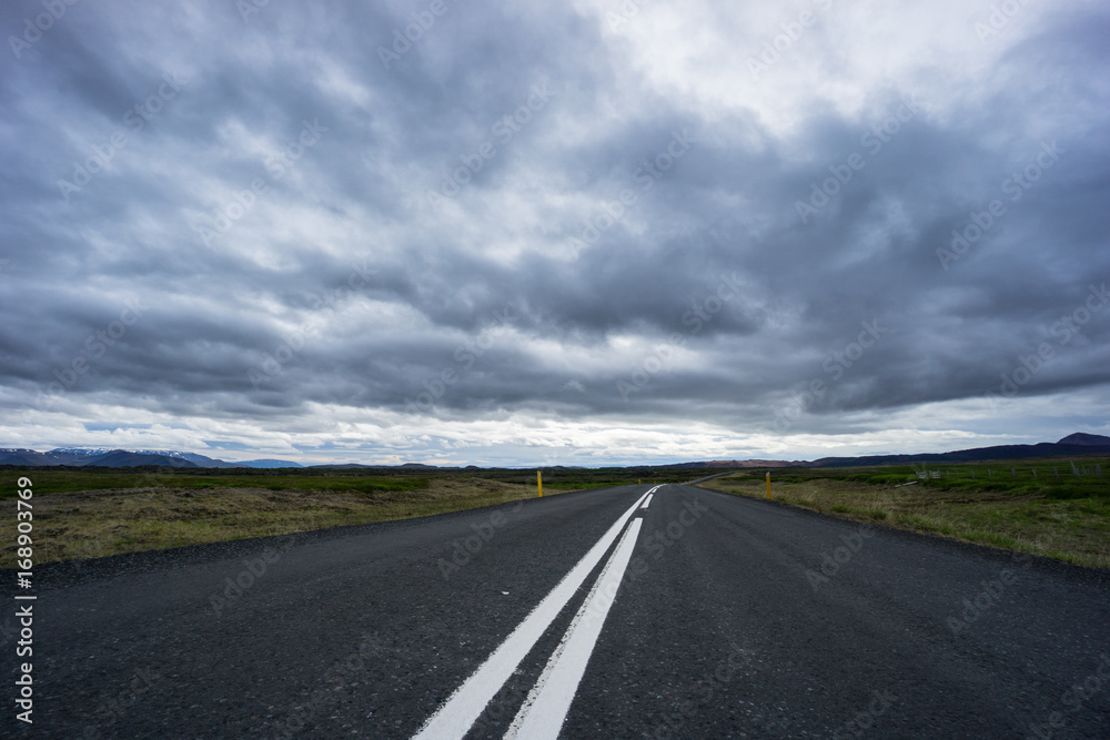 Iceland - Endless street through mountainous landscape and green meadows with cloudy sky