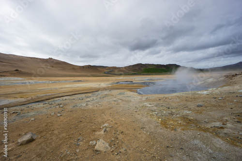 Iceland - Boiling hot mud pot at geothermal area hverir with volcanic colorful mountains