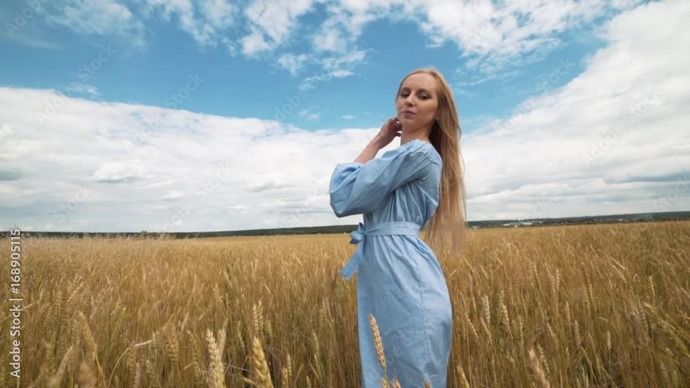 A young girl in a blue dress is standing in the field, and the wind is fluttering her hair A young girl in a blue dress is standing in the field, and the wind is fluttering her hair