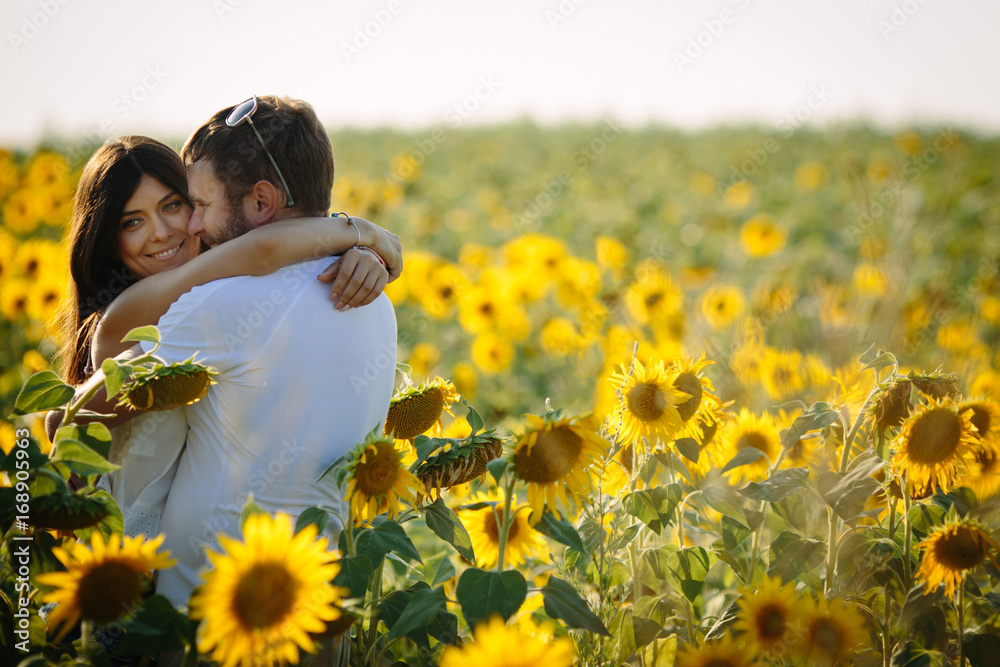 Cute woman hugging her husband in the yellow field of sunflowers, summer Cute woman hugging her husband in the yellow field of sunflowers, summer