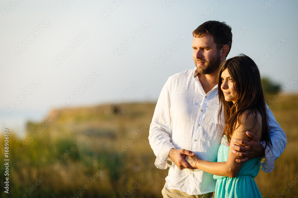 A man and a woman look out into the distance, standing by the shore of the lake