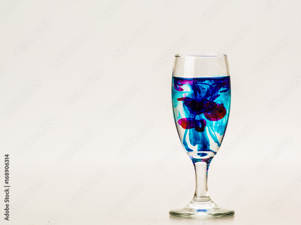 mixture of food coloring diffuse in water inside wine glass with empty copyspace area for slogan or advertising text message, over isolated grey background. mixture of food coloring diffuse in water inside wine glass with empty copyspace area for slogan or advertising text message, over isolated grey background.