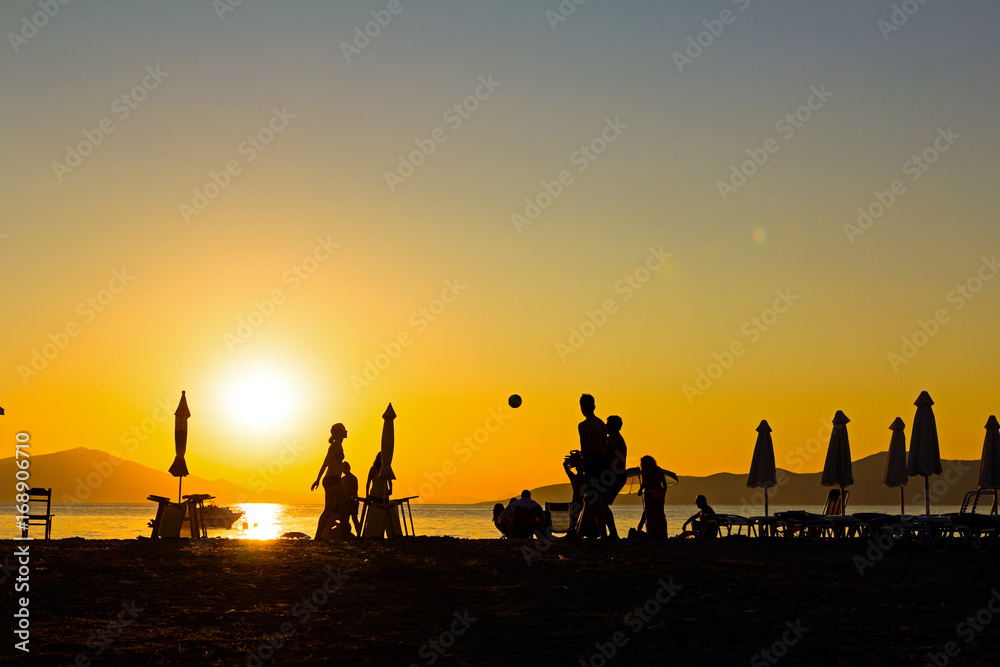 Silhouetted shot of young people are having fun on beach and playing football