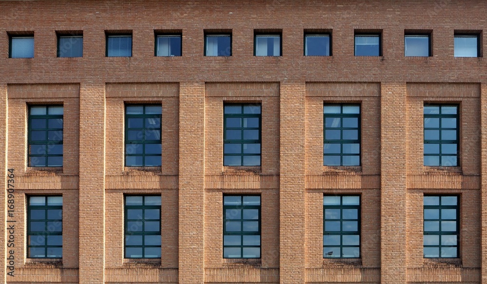 
Brick facade of a modern building with wide  windows and a row of small square windows at the top