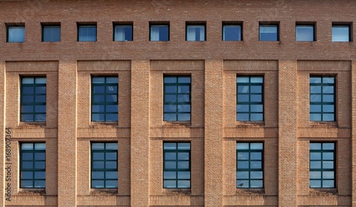  Brick facade of a modern building with wide windows and a row of small square windows at the top
