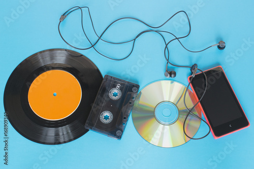 Evolution of technology concept, vinyl record, tape, disk and smartphone with headphones on the blue background. photo