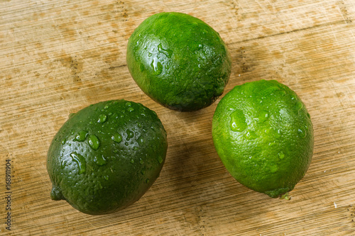 Three green lemons on a wooden plate