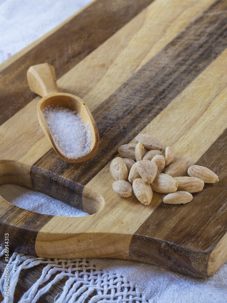 salted almonds with wooden scoop with salt on wooden cutting board salted almonds with wooden scoop with salt on wooden cutting board