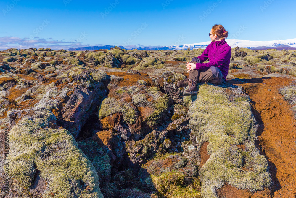 Young woman hiker sitting on rock at mossy lava field near Vik, Iceland